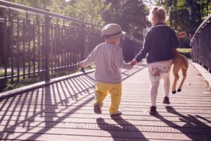 two children holding hands and walking across a bridge