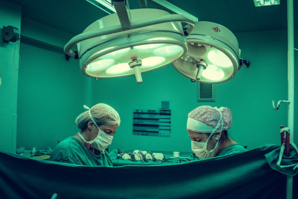 photo depicting two doctors in surgical masks and hairnets operating on an unseen person behind a privacy sheet